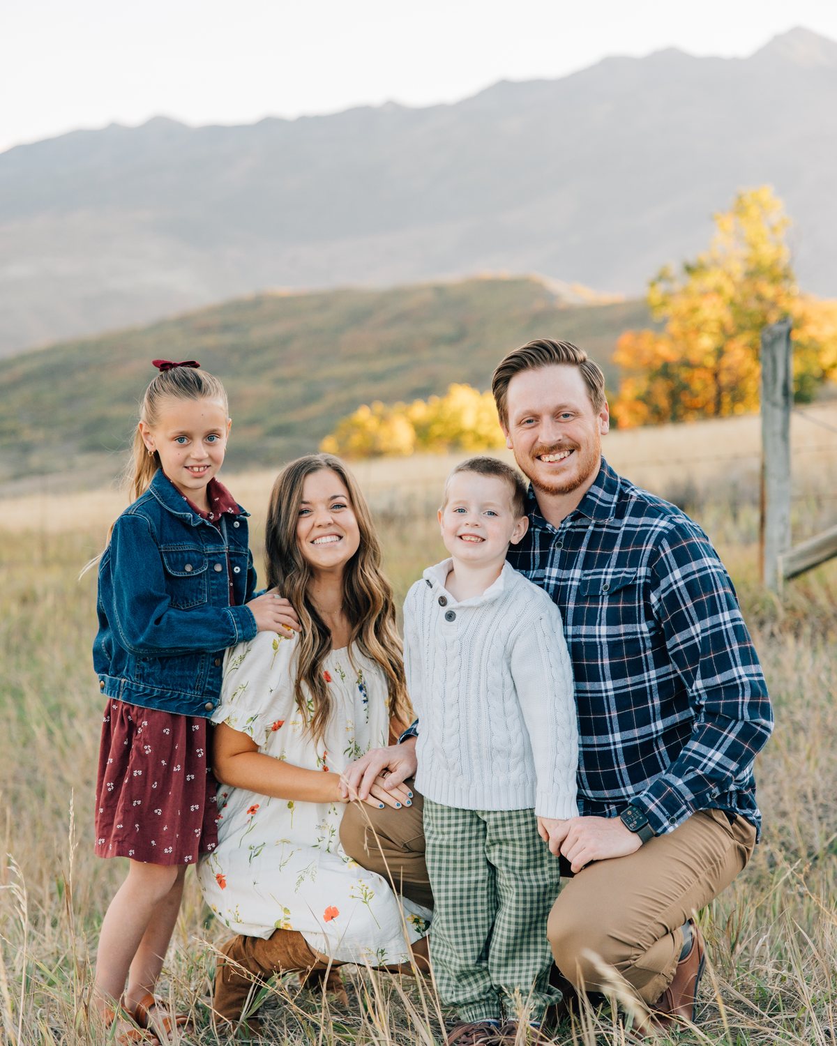 Caleb and Jalen Hutchinson kneeling in a fall field with their two kids, mountains behind them